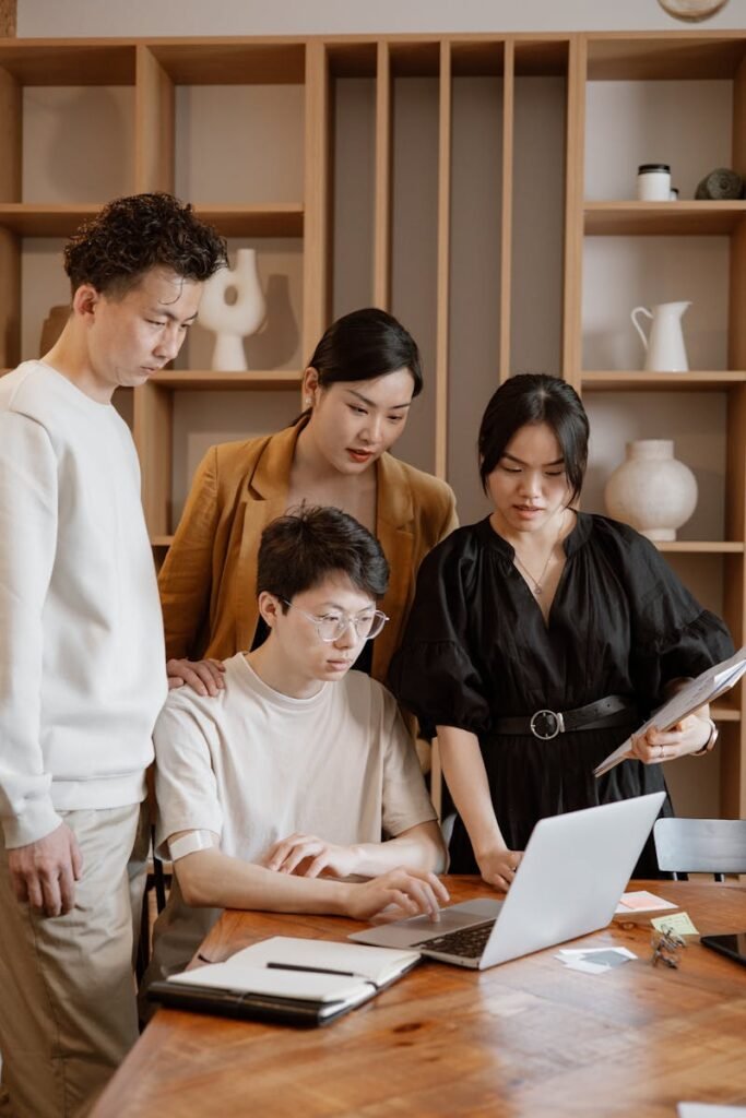 A group of Asian professionals engaged in collaborative work around a laptop in an office setting.